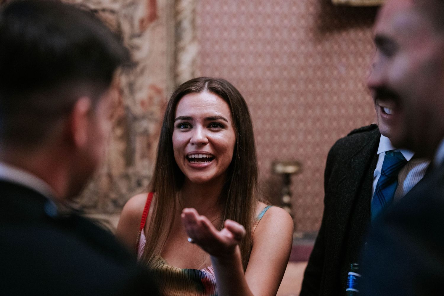 Wedding guests share laughter and conversation at an elegant indoor reception venue.