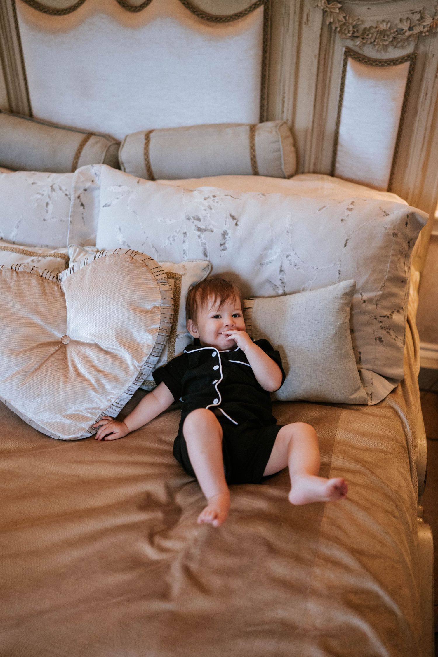 A small child relaxes on a beige couch with decorative pillows in an elegant room setting.