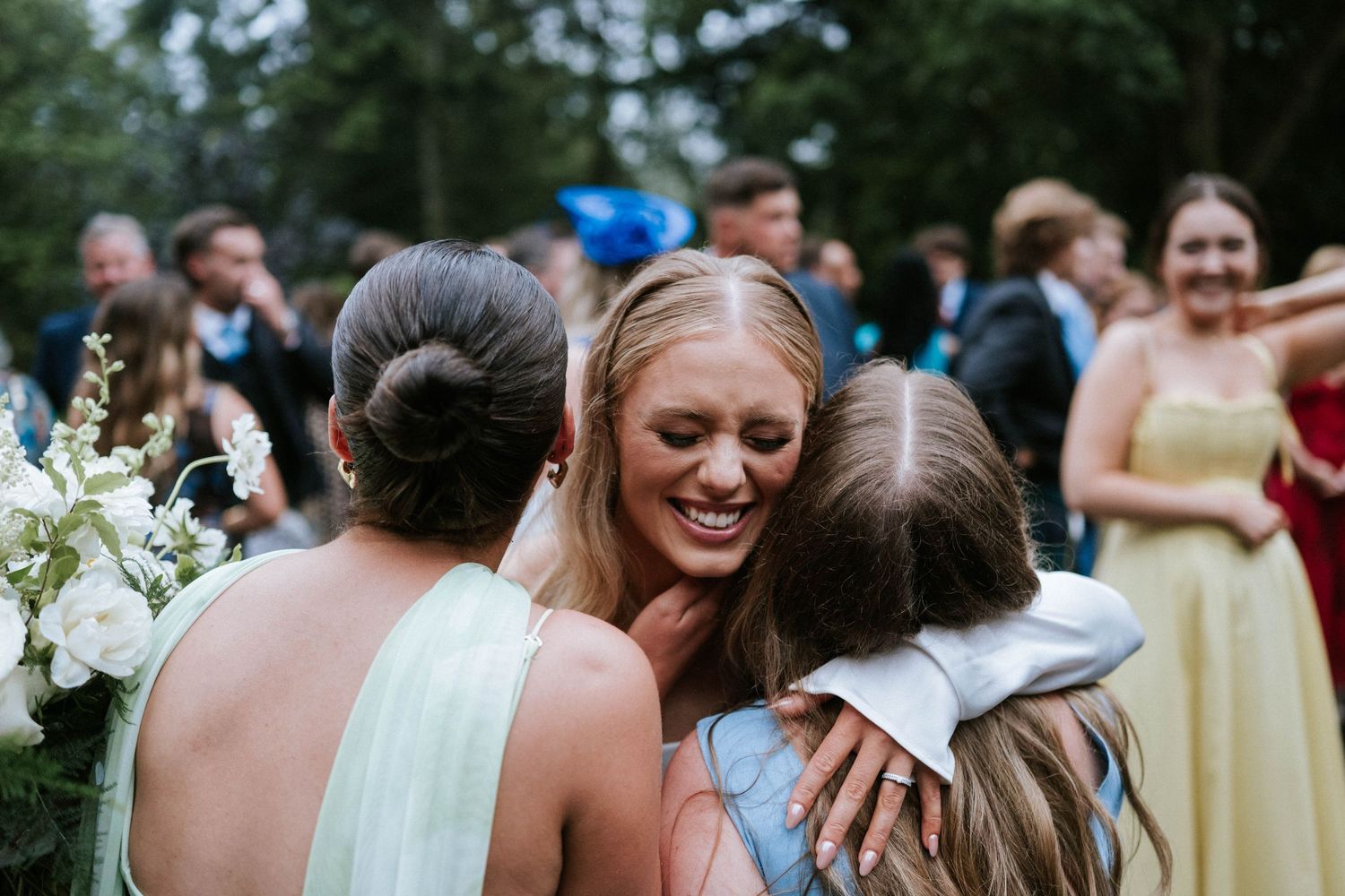 Wedding guests celebrating and embracing outdoors during a sunny reception.