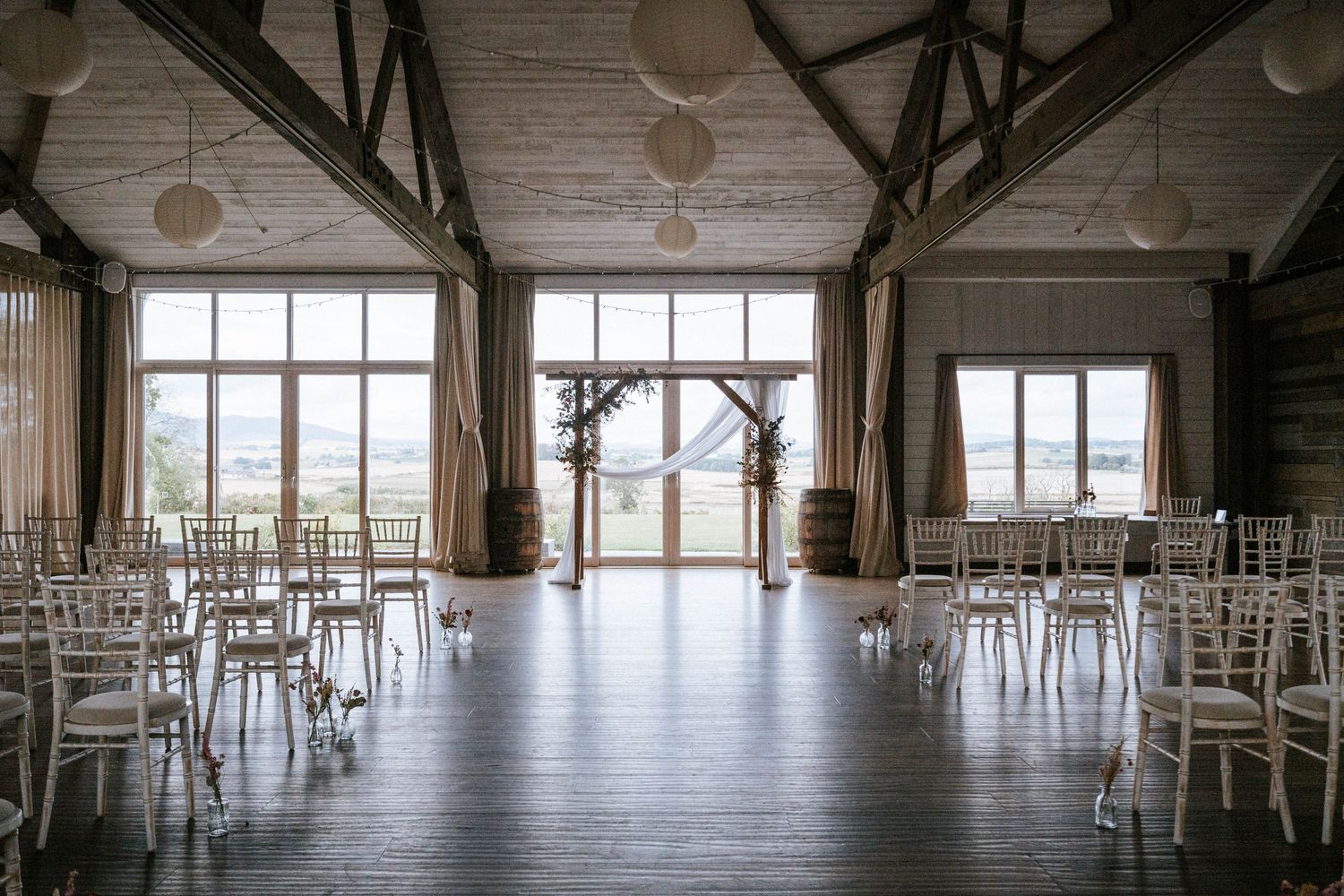 Large empty event venue with white chairs arranged in rows and hanging paper lanterns creating an elegant atmosphere.