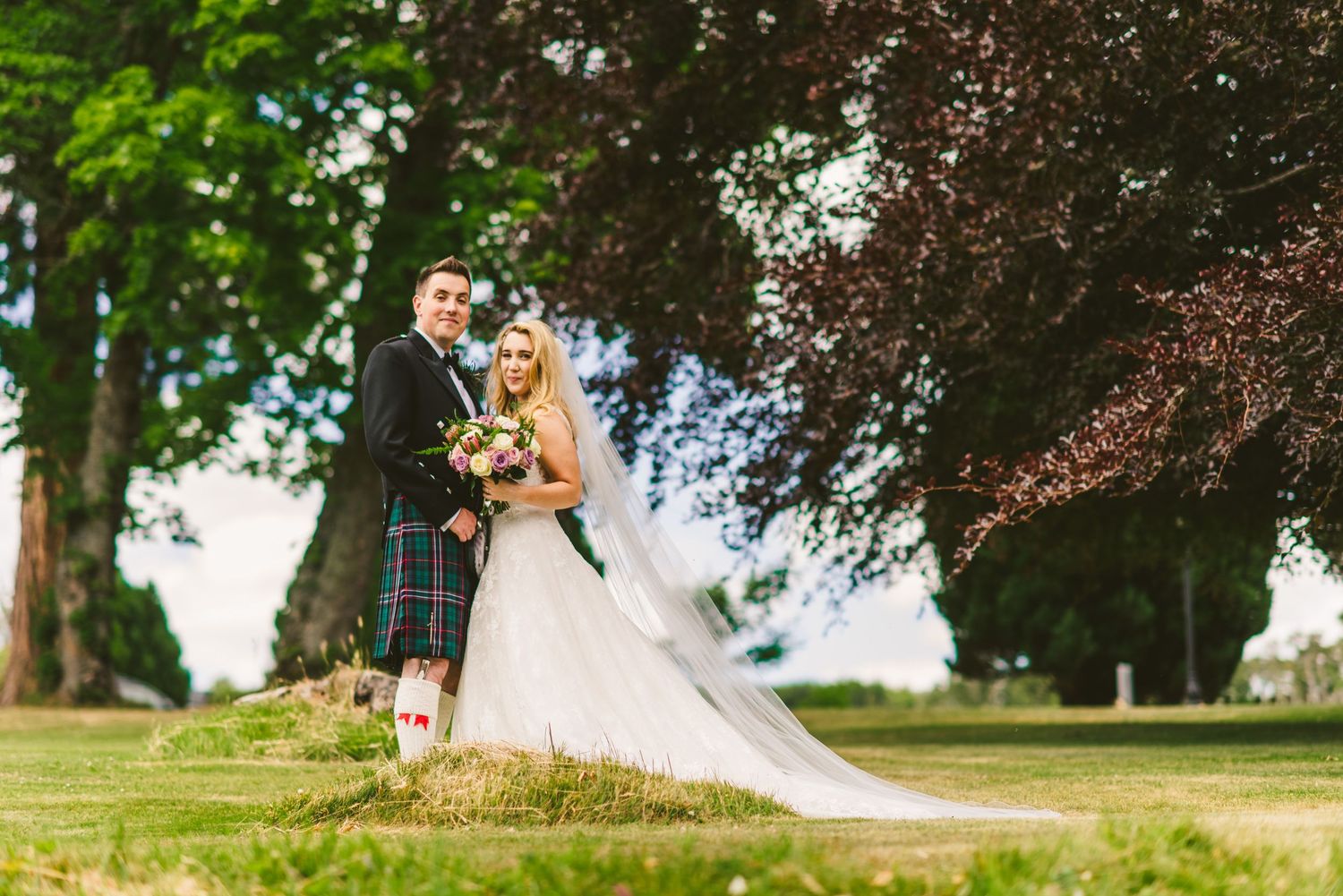 Newlyweds walking through lush garden setting with trees and greenery.