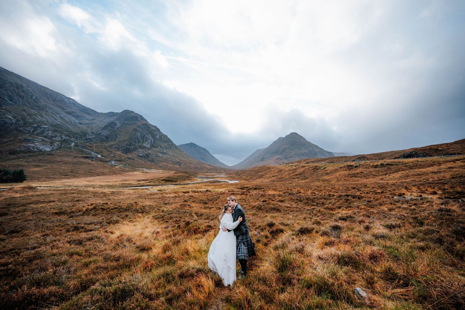 A wedding couple stands in a dramatic mountain landscape with misty peaks and autumn colors.