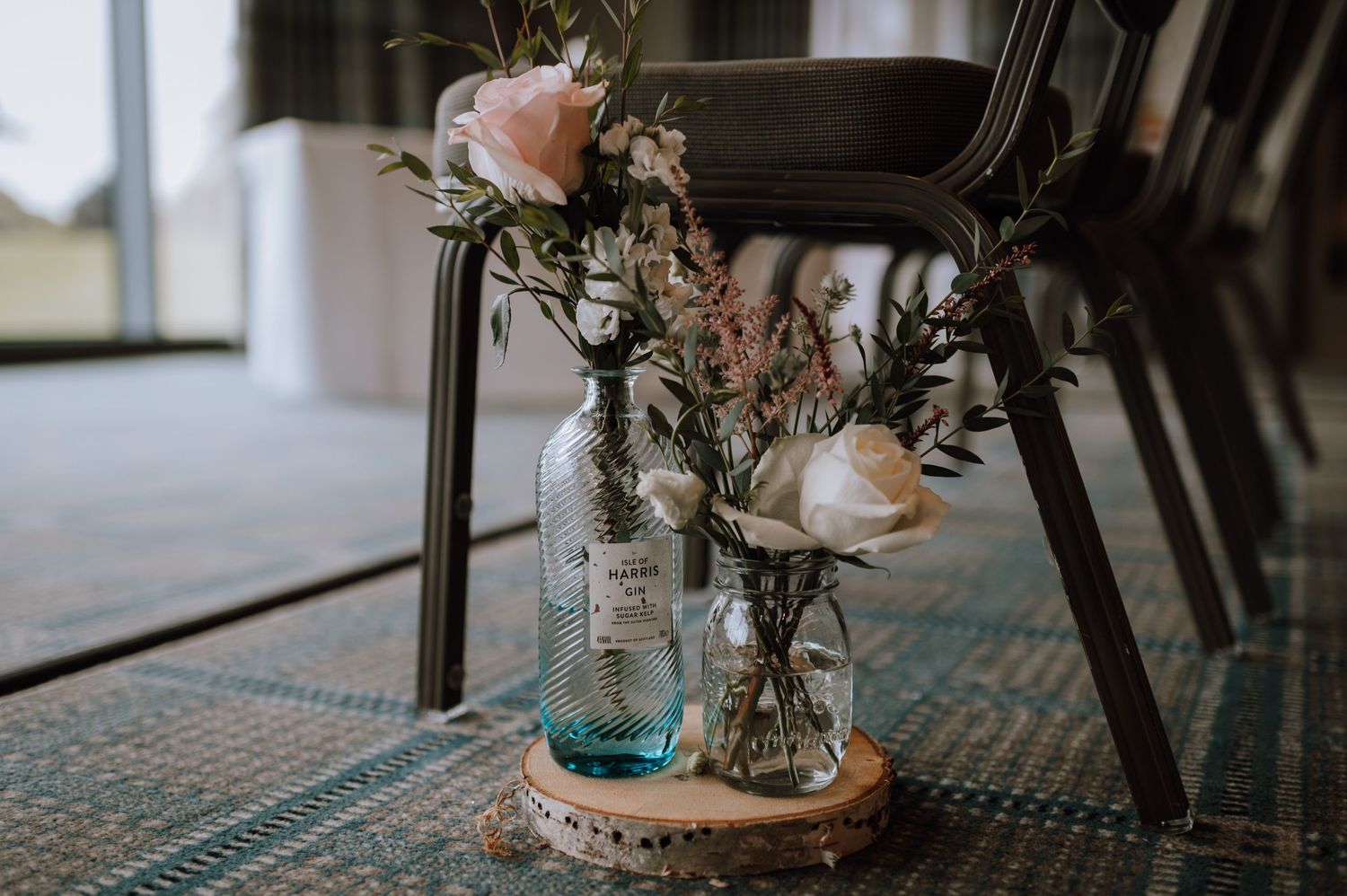 Vintage mason jars filled with pink roses and greenery sit on a wooden coaster.