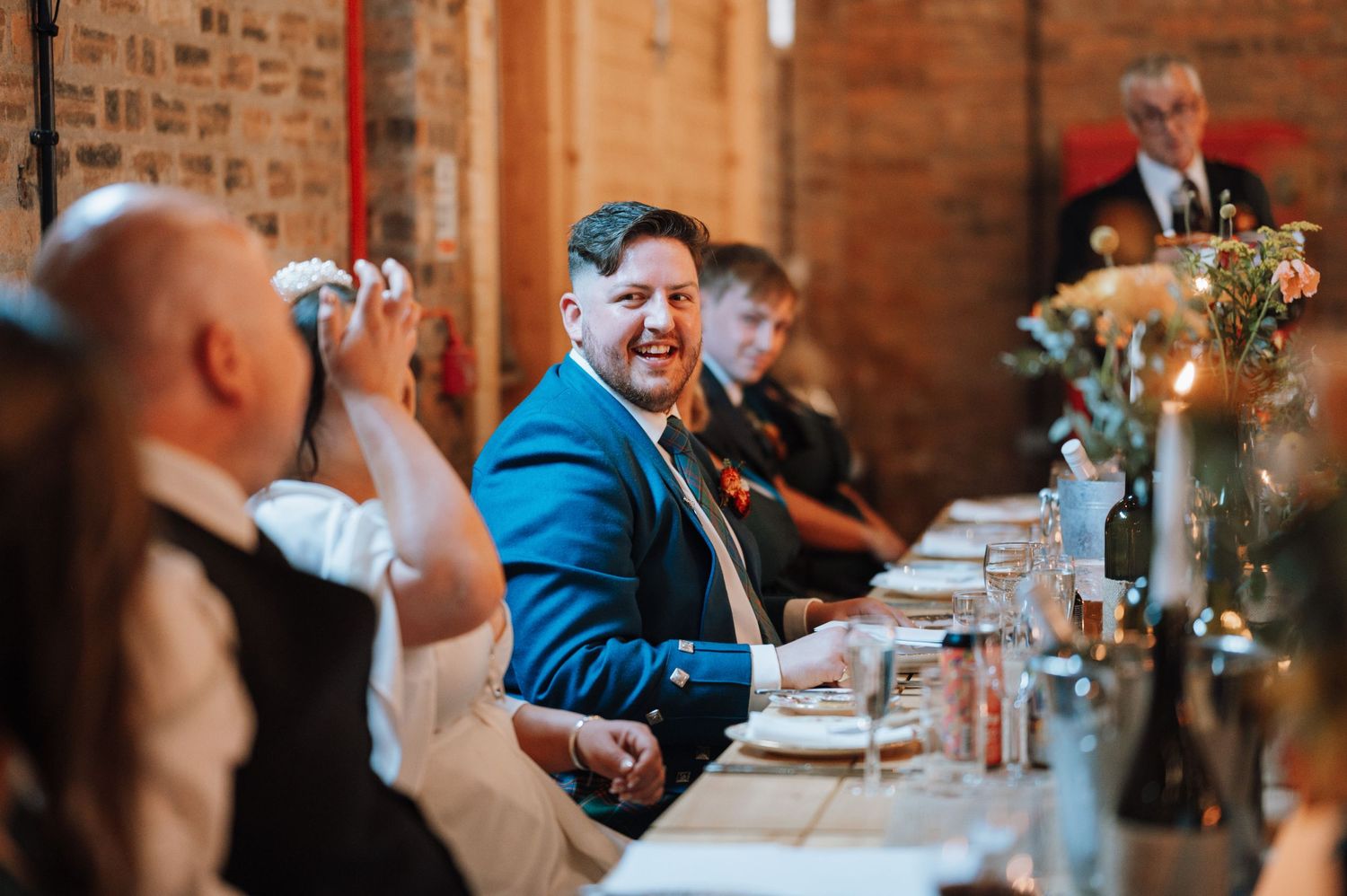 Guest in bright blue suit jacket socializes at wedding reception dinner table.