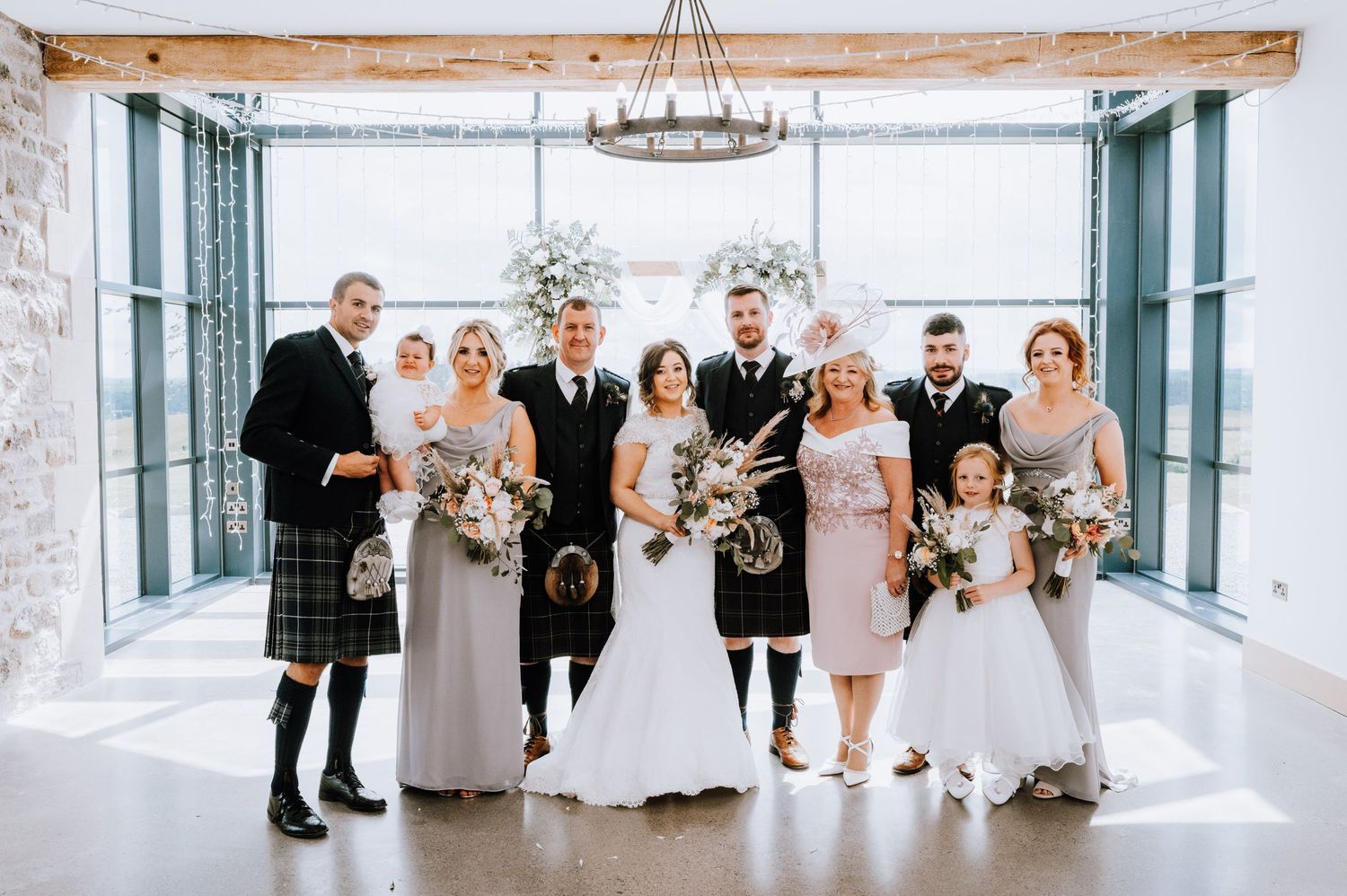 Wedding party poses in bright indoor venue with stone walls and large windows.