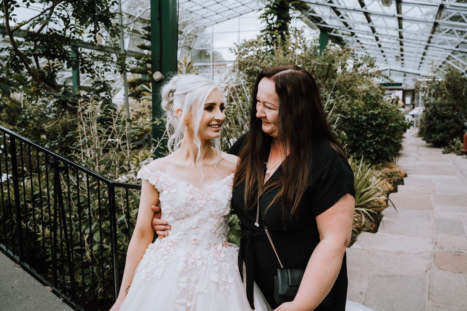 Two people share a moment in a greenhouse setting with lush greenery.