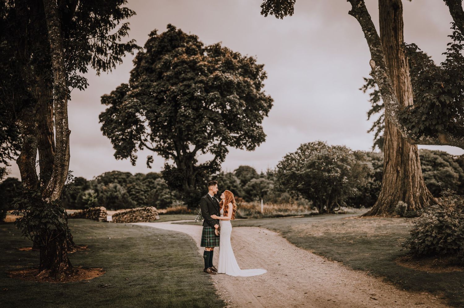 A couple shares an intimate moment on a tree-lined path during their Scottish wedding photoshoot.