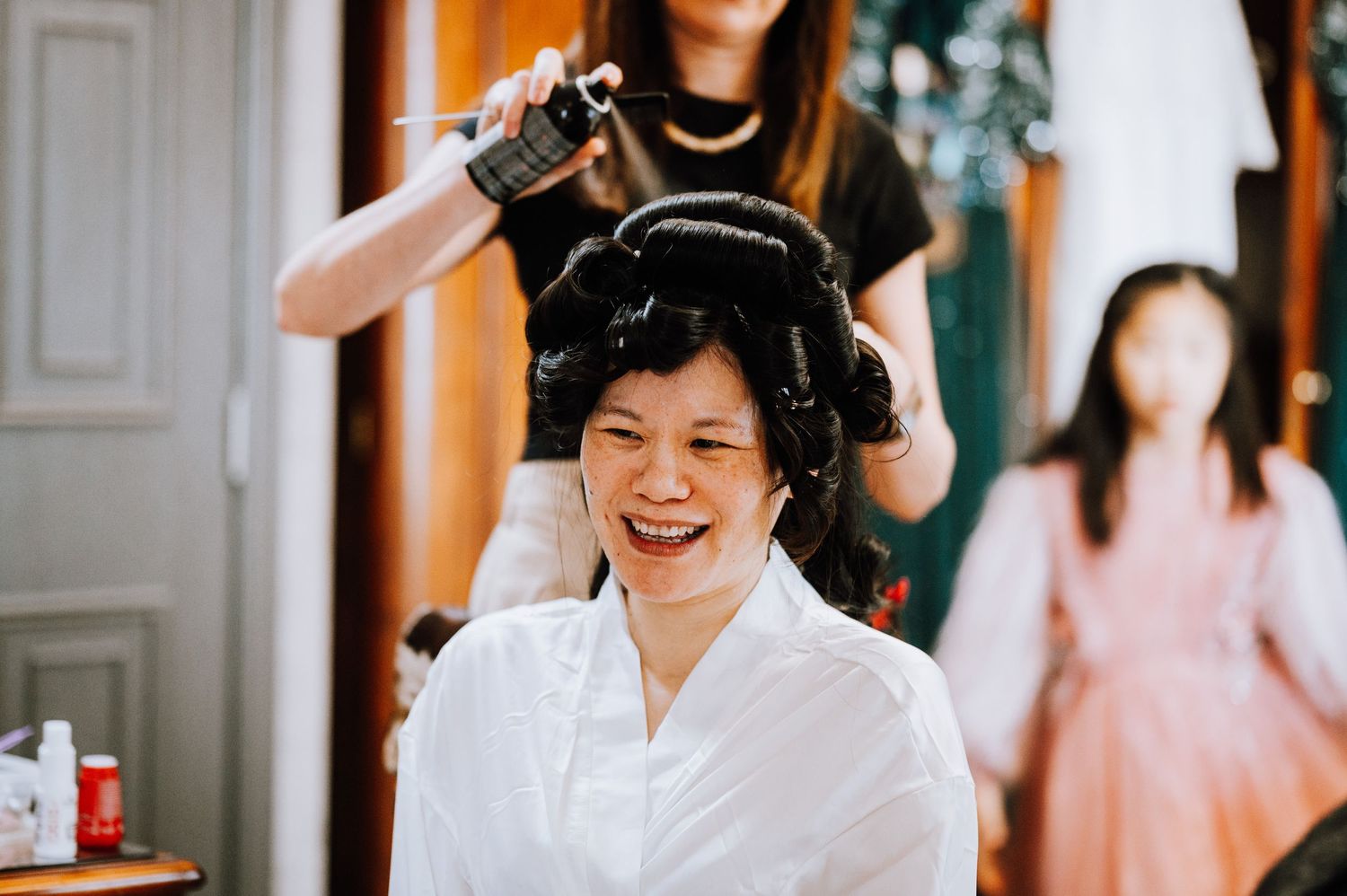 Person getting hair styled while wearing white robe and laughing joyfully.