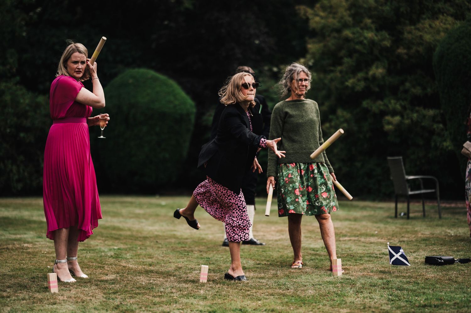 Three women in colorful dresses playing outdoor lawn games at a garden party.