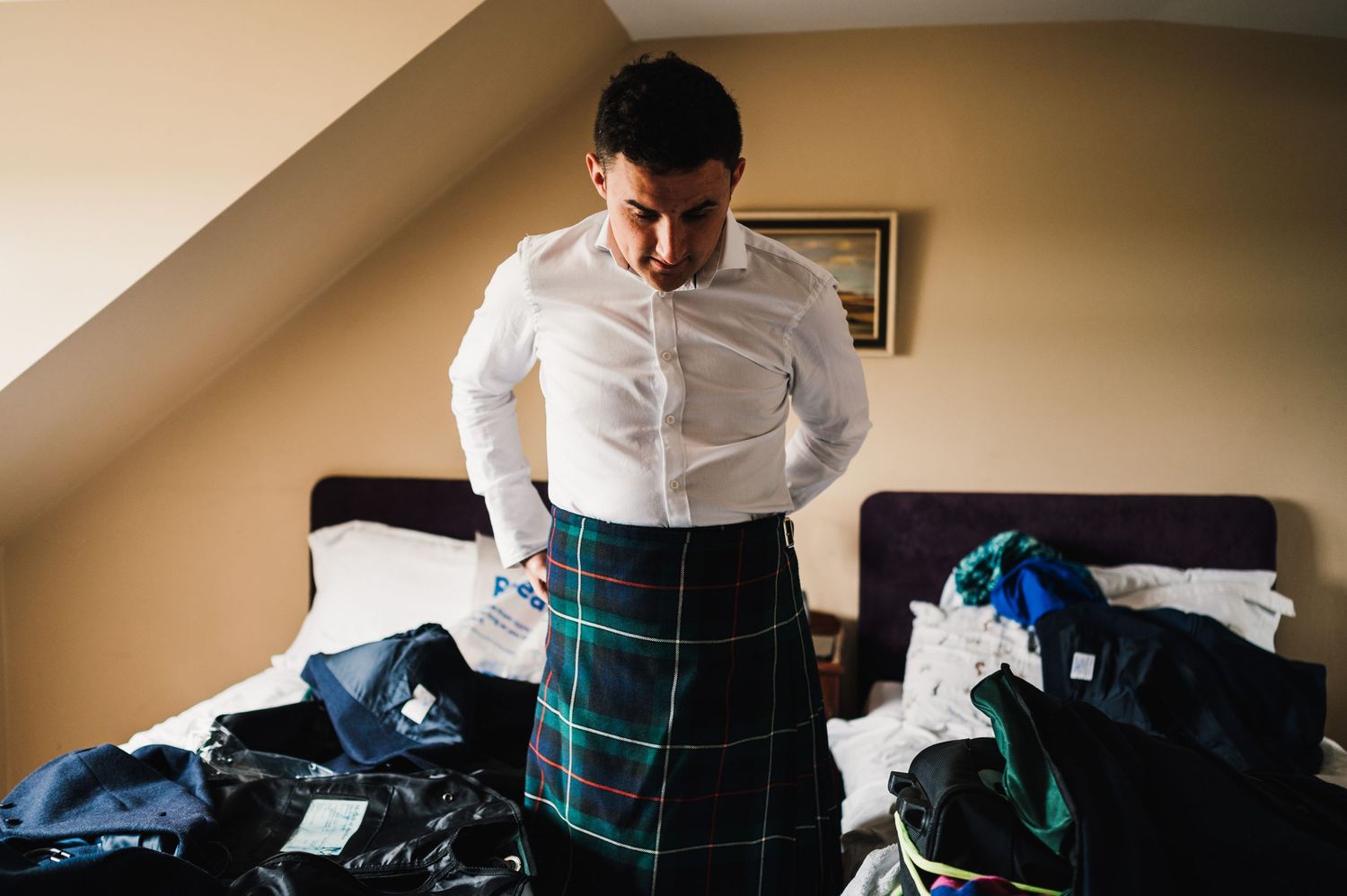 Person adjusting traditional Scottish tartan kilt while getting ready in bedroom.
