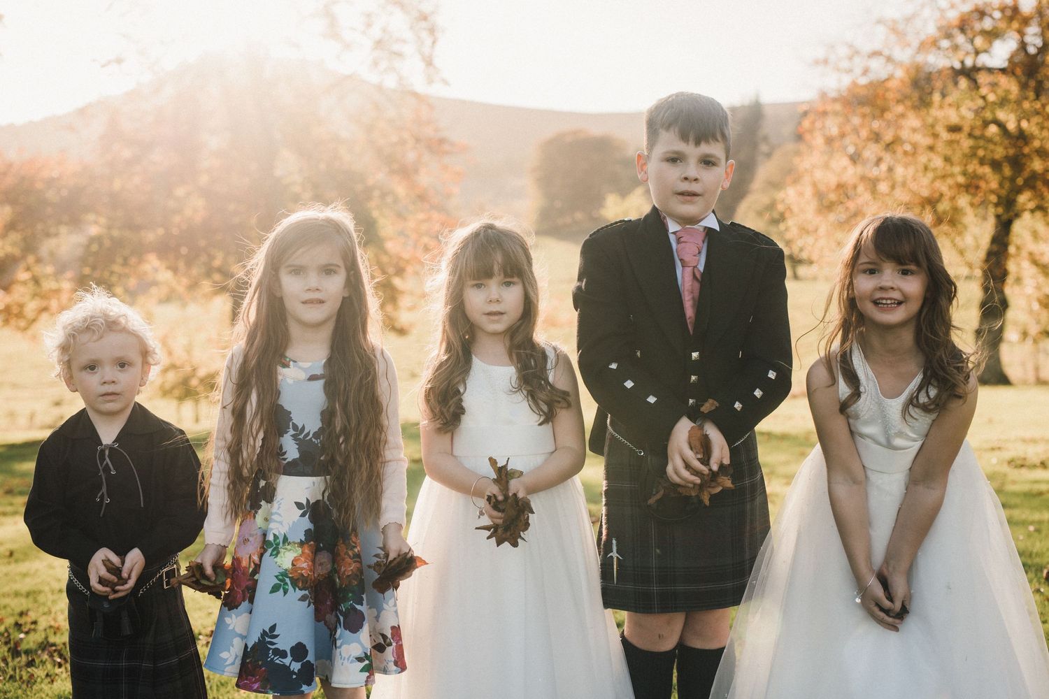 Children in formal attire pose together at sunset during a wedding celebration.