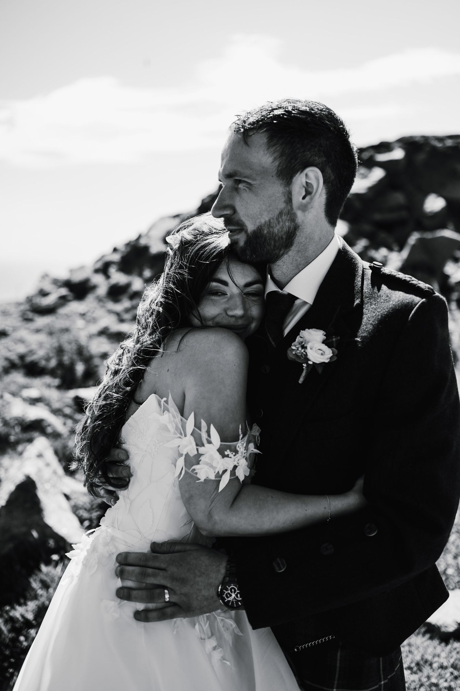 Black and white portrait of newlyweds embracing against dramatic rocky landscape.