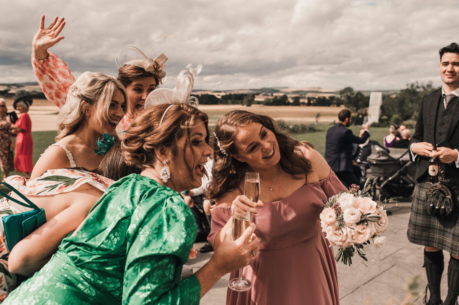 Wedding guests celebrate joyfully outdoors with windy hair and colorful dresses.