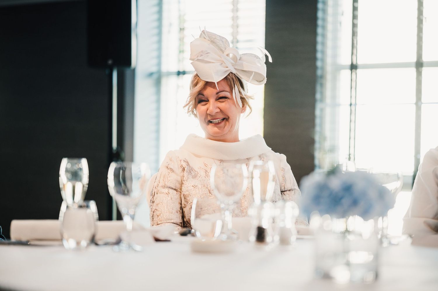A wedding guest in formal attire smiles while seated at a decorated reception table.