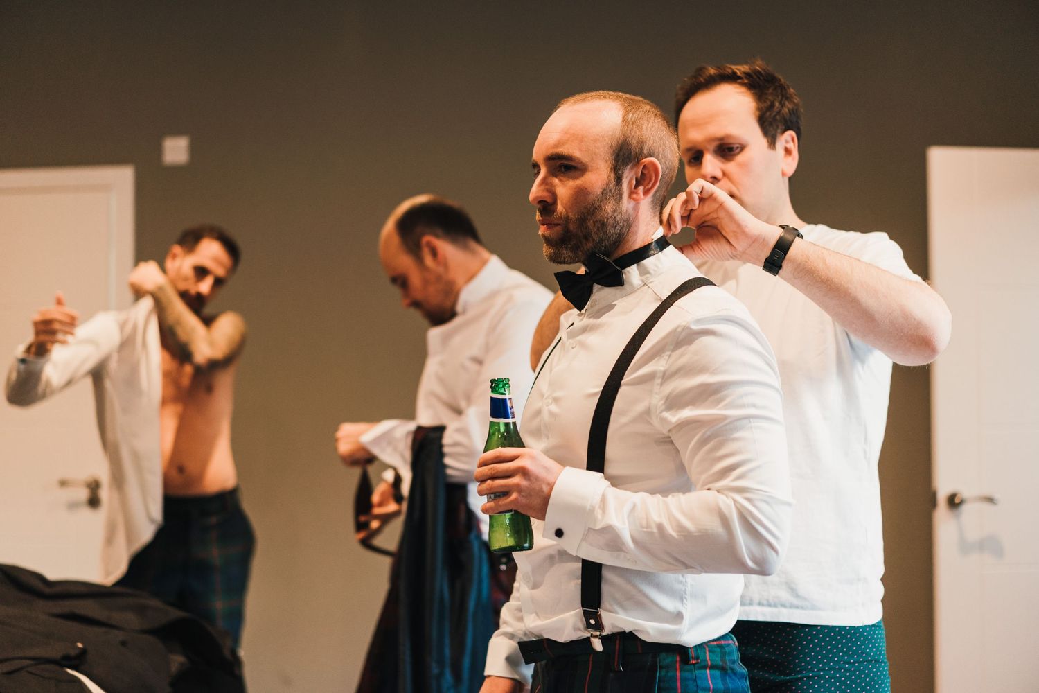 Wedding party members enjoying drinks while getting dressed in formal attire.