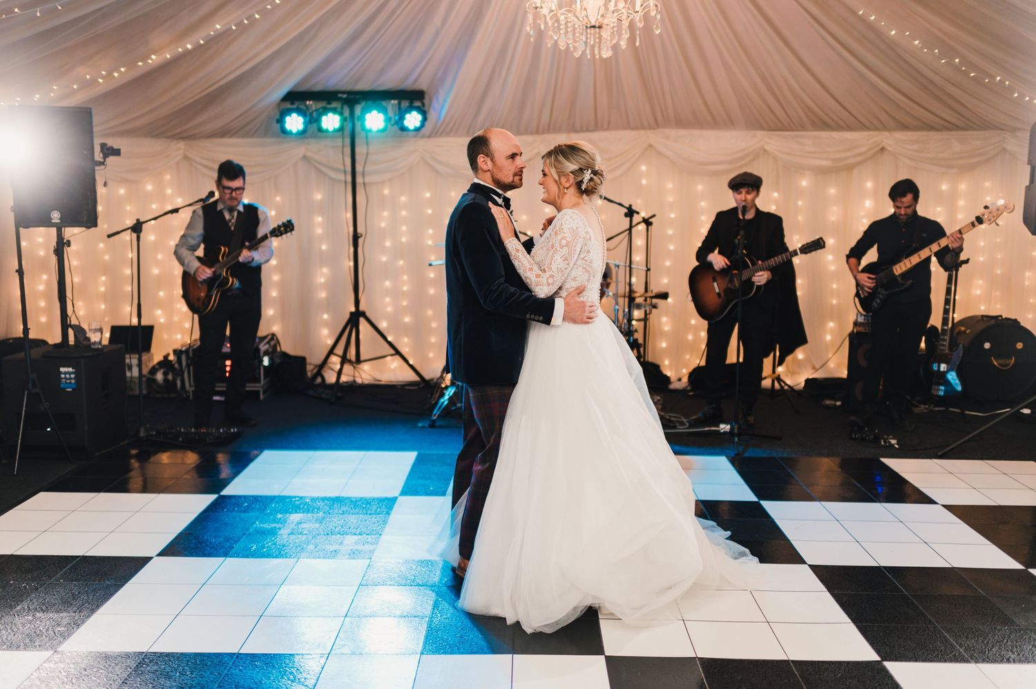A couple shares their first dance on a checkered floor with a live band performing.