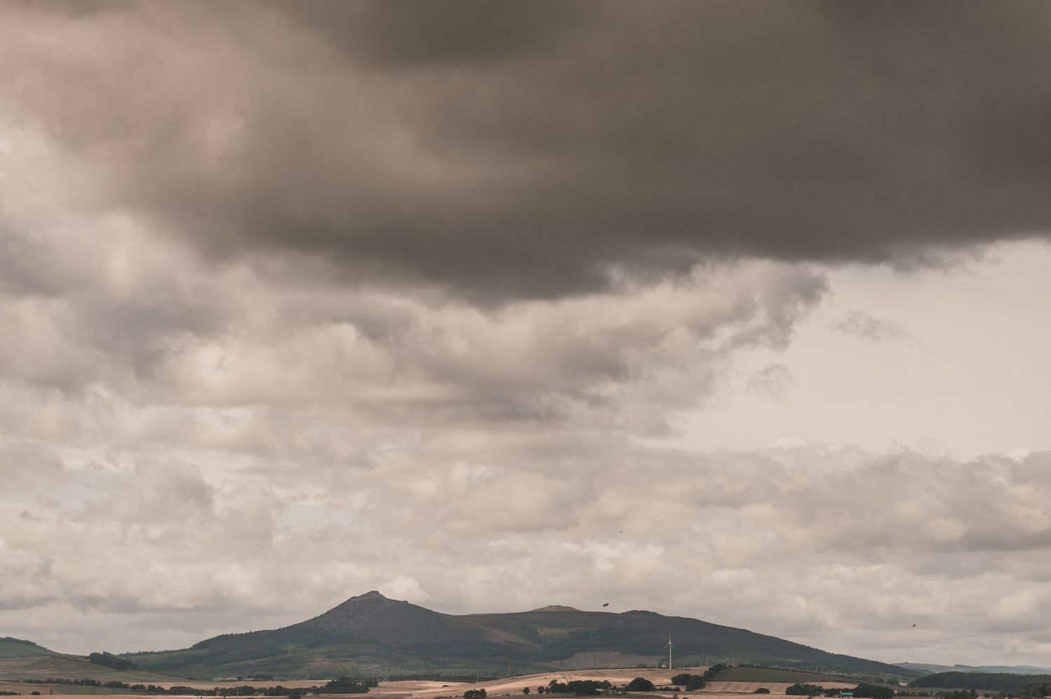 Dramatic cloudy sky over mountain landscape with rolling hills in muted sepia tones.