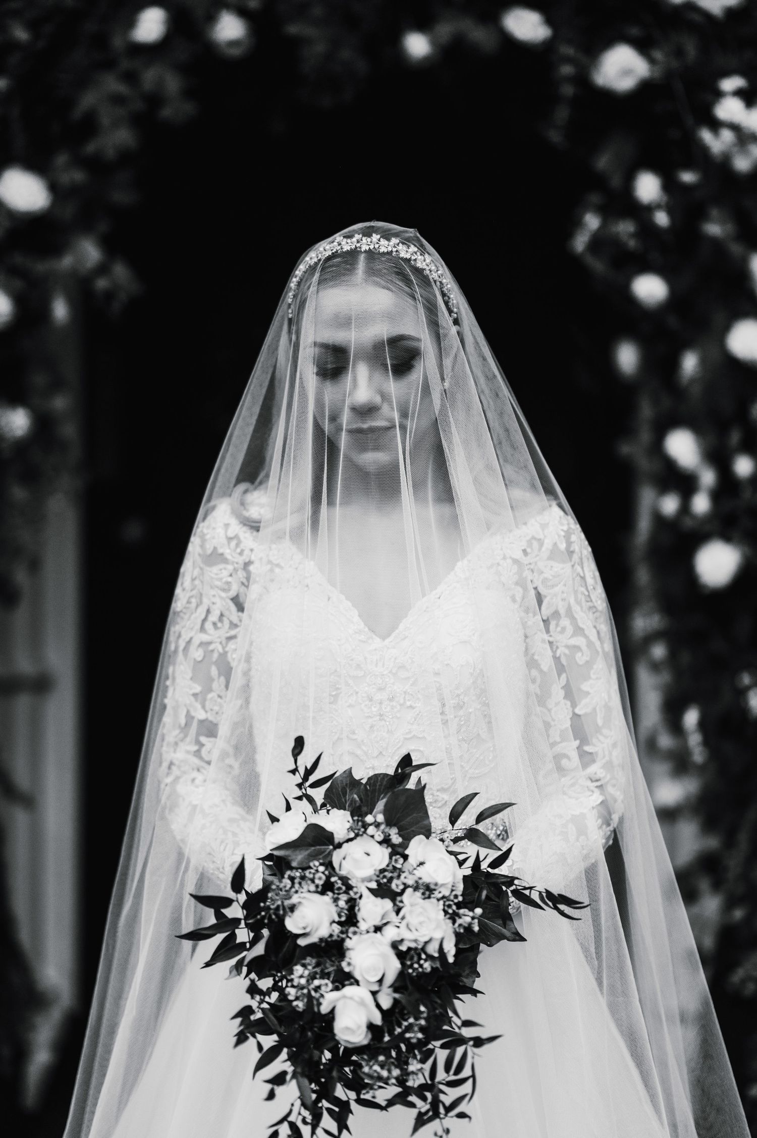 A stunning black and white portrait of a bride in a lace veil holding an elegant bouquet of white flowers.