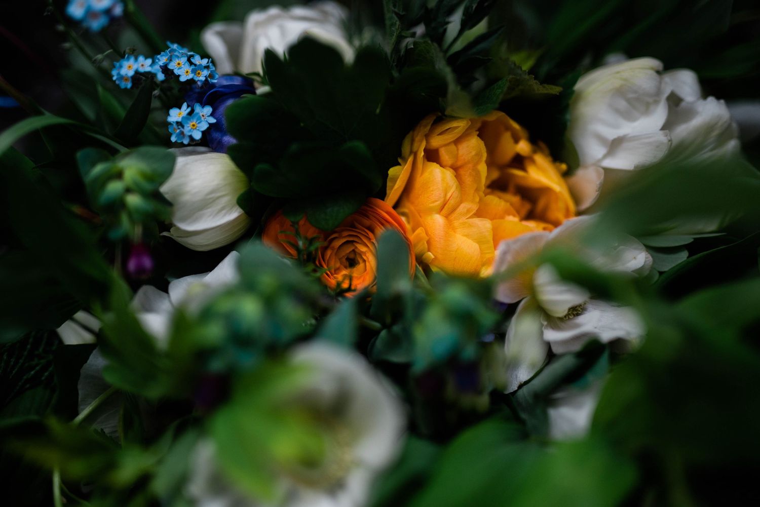 Close-up of an orange rose surrounded by white flowers and greenery in a wedding bouquet.