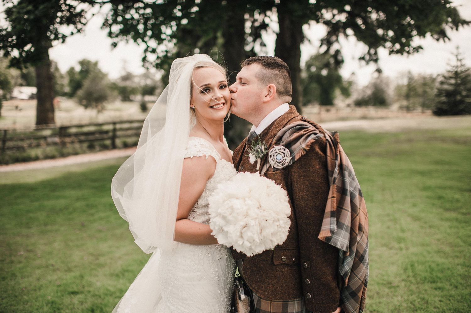 Close-up of wedding couple sharing tender moment outdoors in Scottish wedding attire.