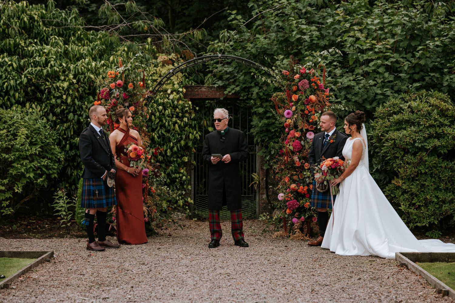 Wedding ceremony taking place in a garden with red floral decorations.