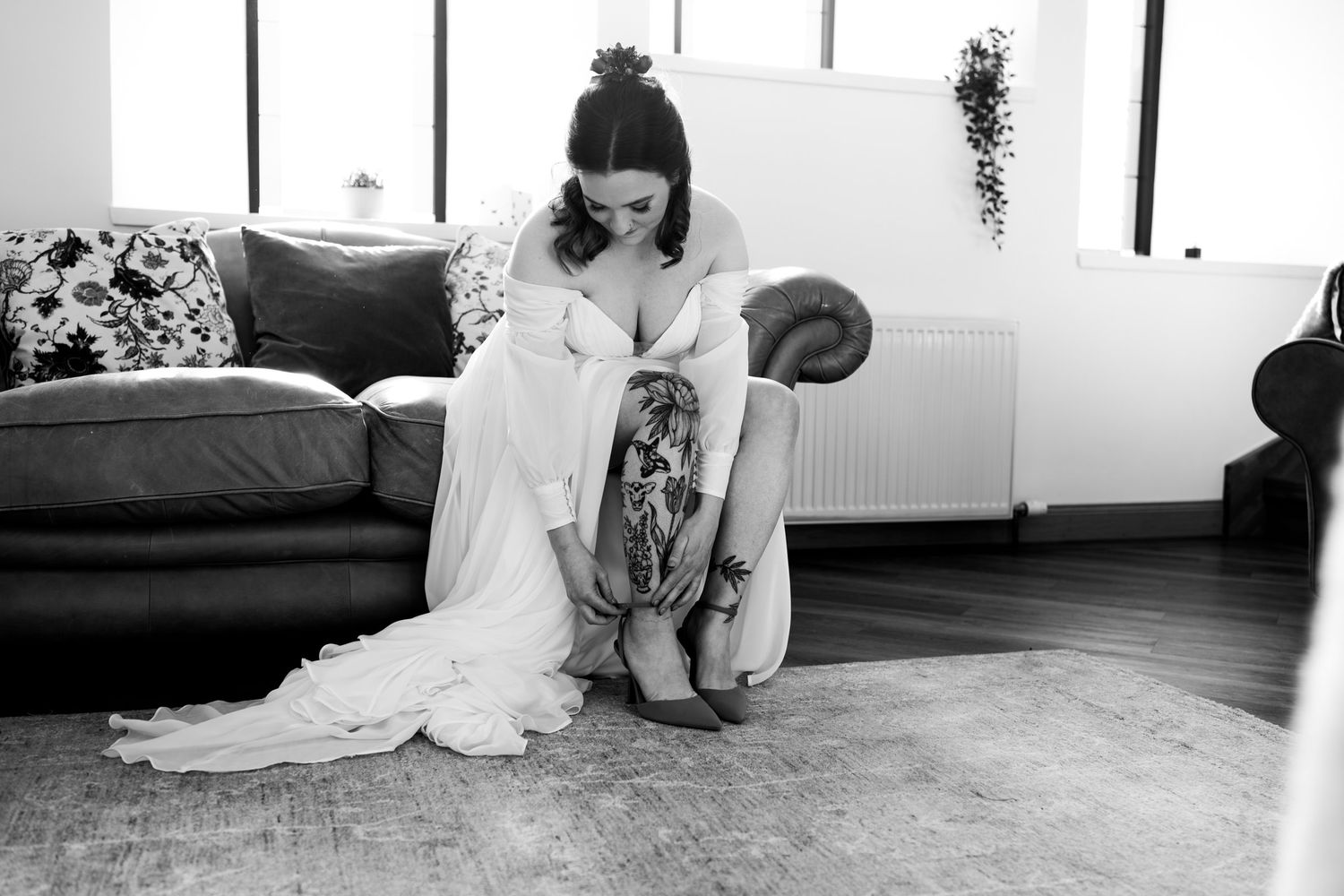A person in a flowing white dress sits on a hardwood floor in a black and white photograph.