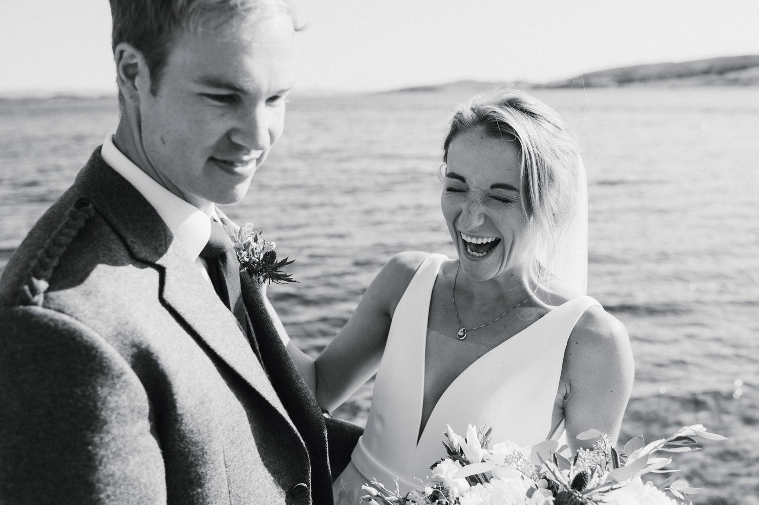 A happy couple shares a joyful moment together by the ocean in black and white.