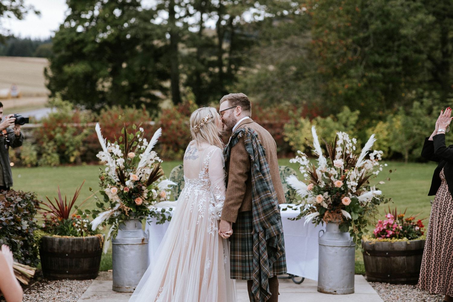 Beautiful floral arrangements with autumn colors decorate a rustic outdoor wedding setting.