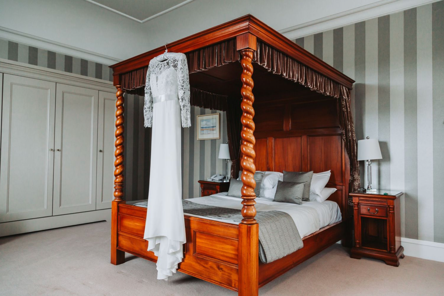 Elegant four-poster bed with white bedding and striped wallpaper in a traditional bedroom interior.