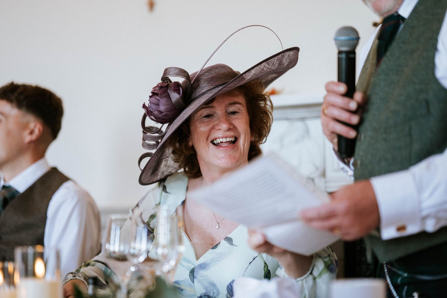 Wedding guests laughing and enjoying speeches during the reception dinner.
