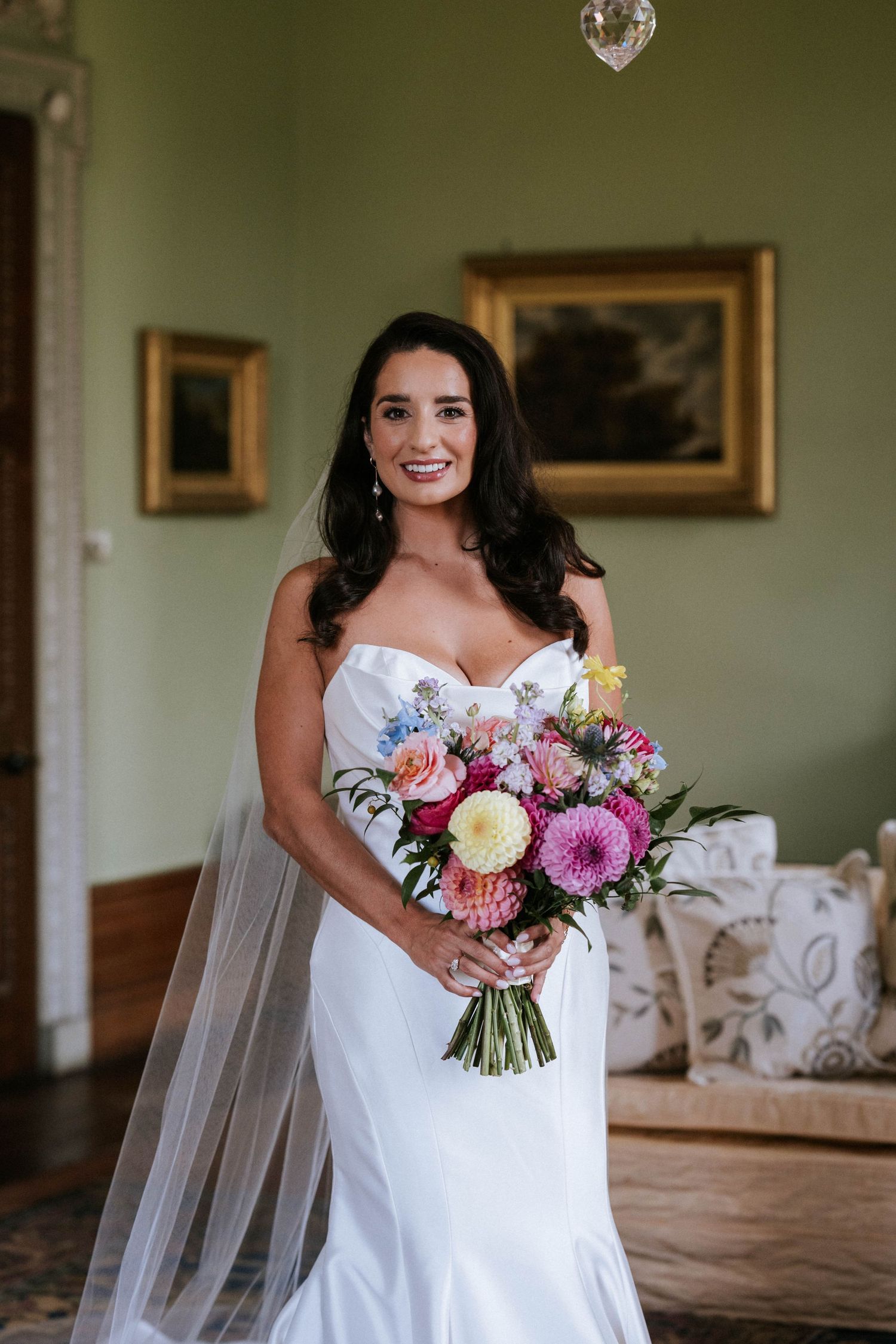 Bridal bouquet featuring pink and purple flowers including dahlias and roses against a light background.