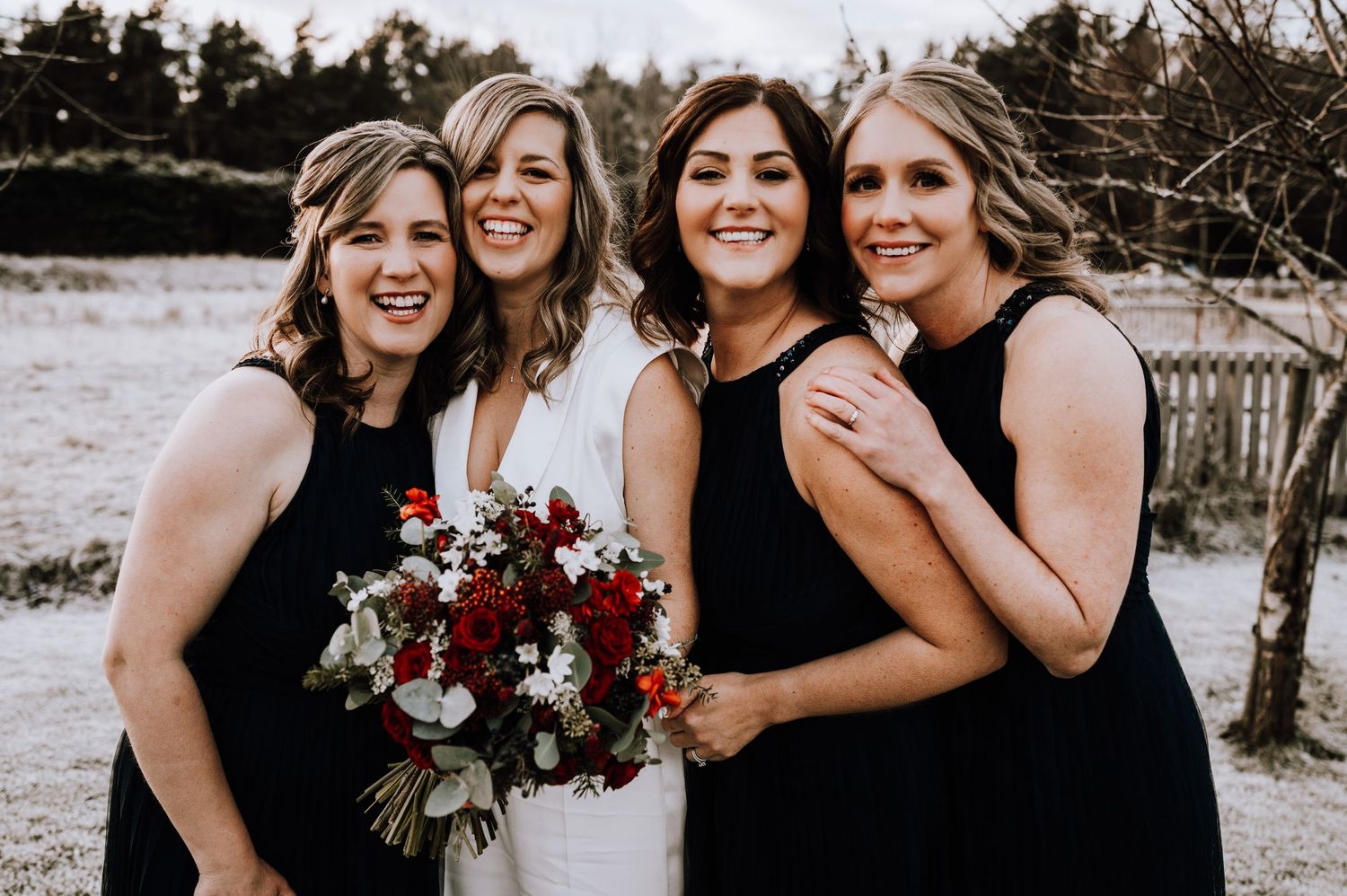 Same Sex Wedding Photography. Wedding party members in black dresses pose together with burgundy bouquet.