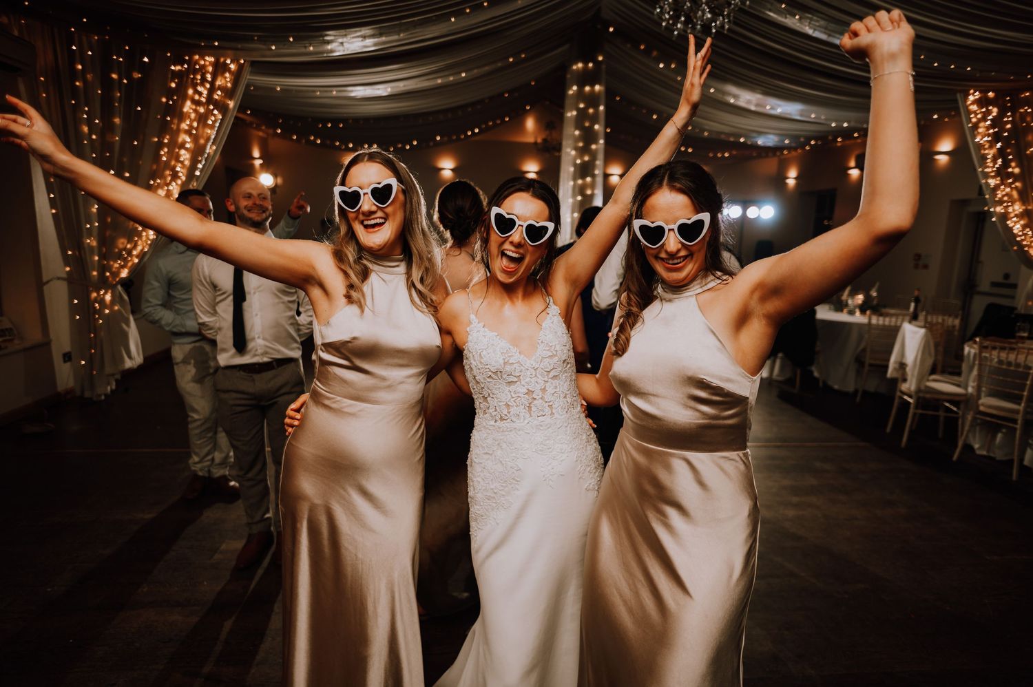 Aberdeen Wedding Photography. People dancing and celebrating with raised arms under draped fabric ceiling and string lights.