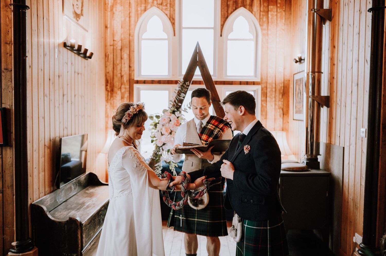 Wedding ceremony in a rustic chapel with Scottish kilts and triangular altar backdrop.
