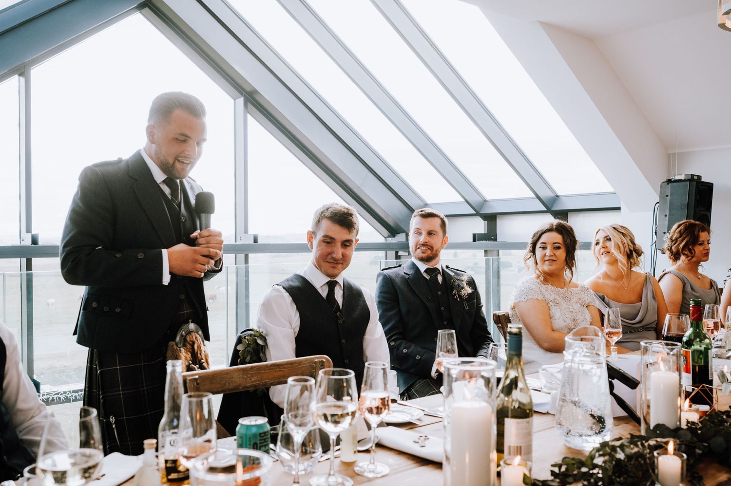 Wedding guests listening to speeches during an elegant reception with skylights.