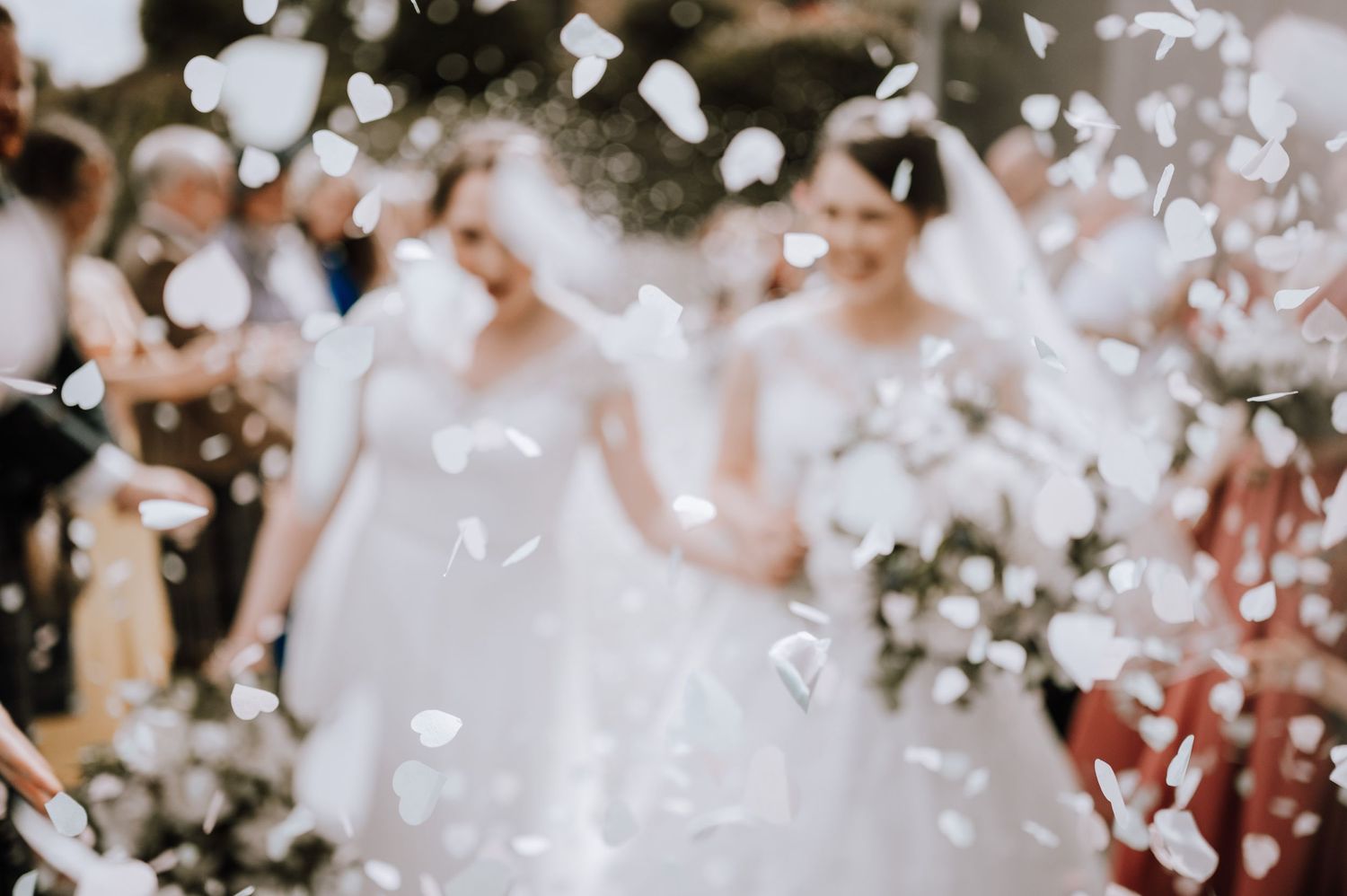 White rose petals fall through the air at an outdoor wedding celebration.