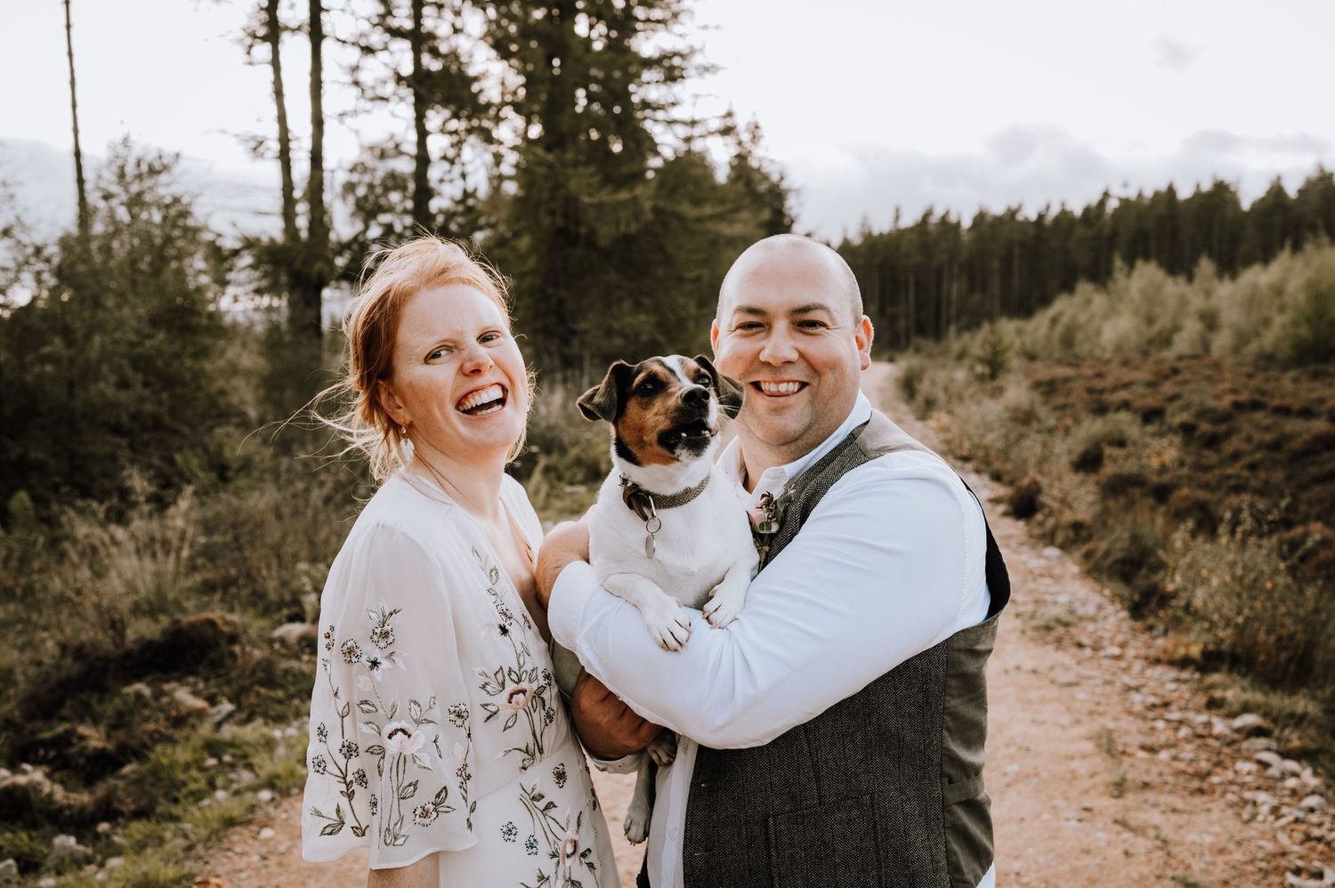Happy wedding couple poses with their small dog on forest trail.