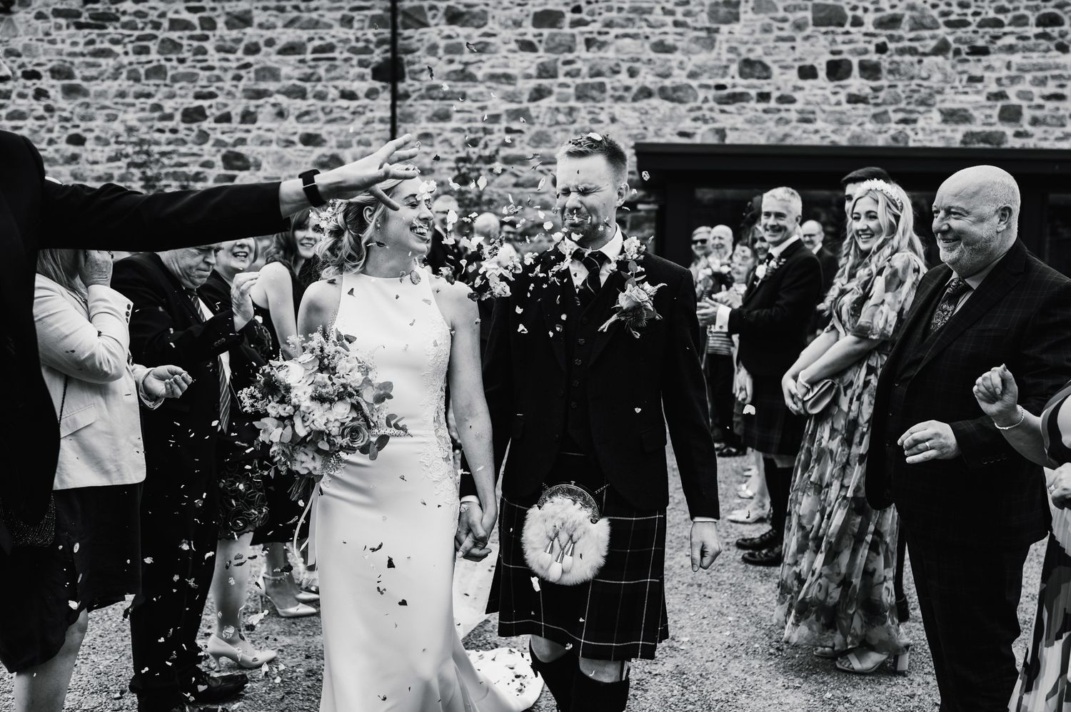 Black and white photo of wedding party gathering outside stone venue.