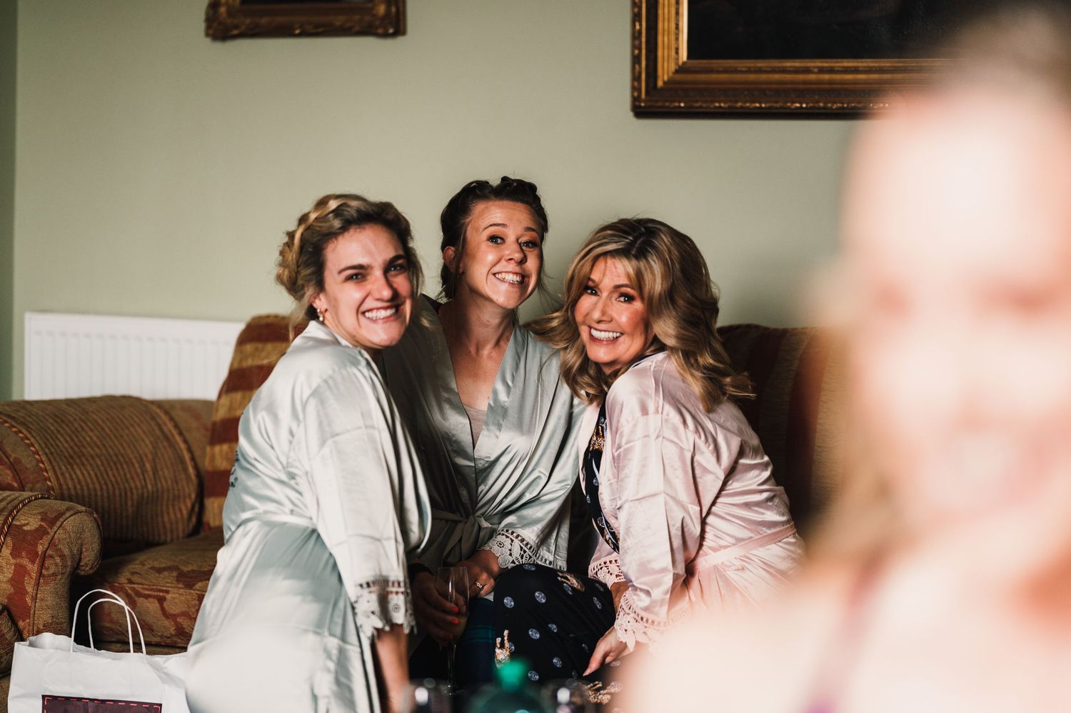 Three people in robes share a joyful moment during wedding preparation.
