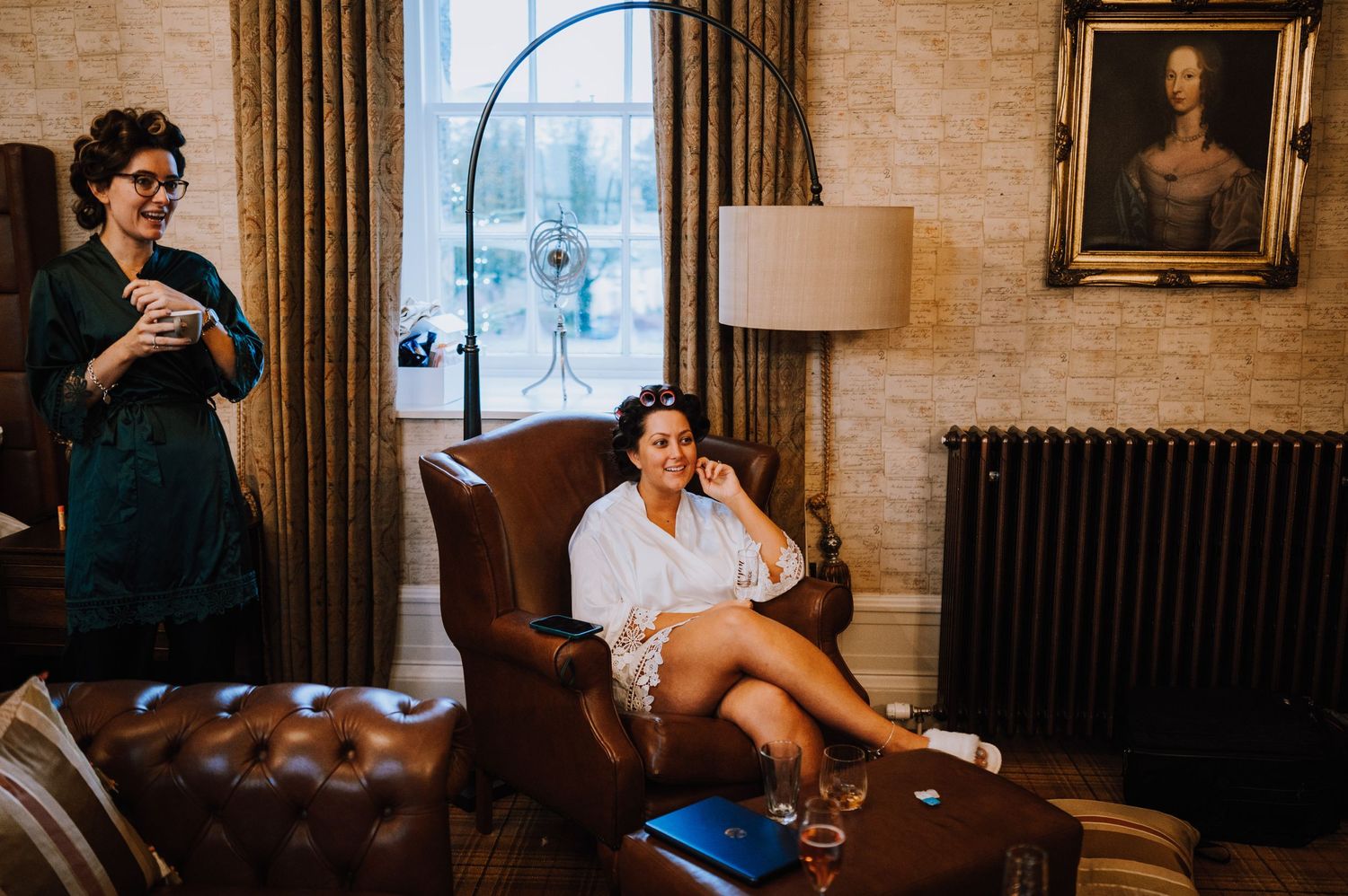 Two people relax in an elegant room with vintage furniture and a portrait on the wall.