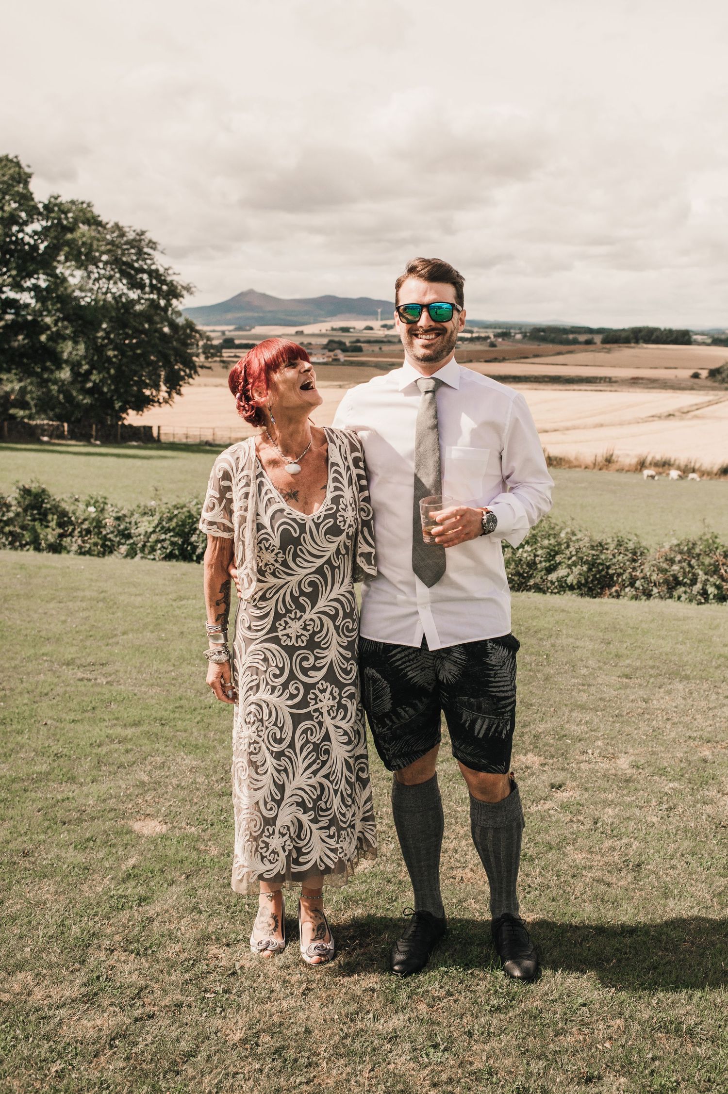 Couple poses on hilltop overlooking scenic countryside, groom wearing shorts and prosthetic leg.