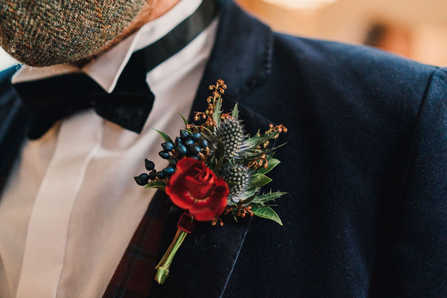 Close-up of red rose and thistle boutonniere on navy suit lapel.