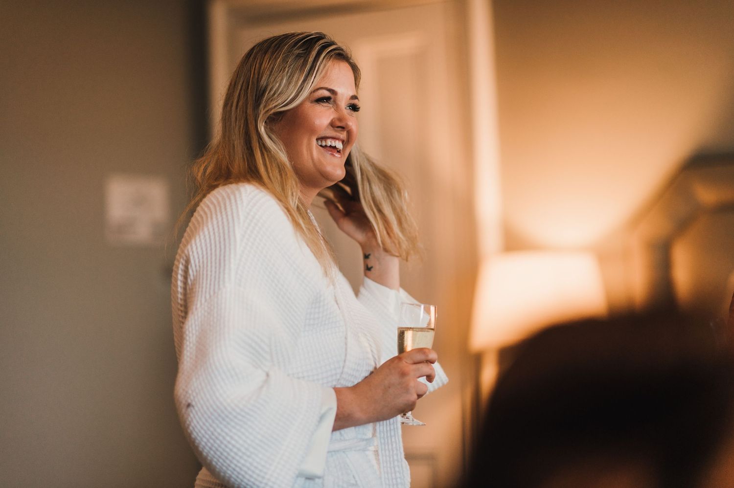 A joyful moment during wedding preparations showing someone in white robe holding a drink.