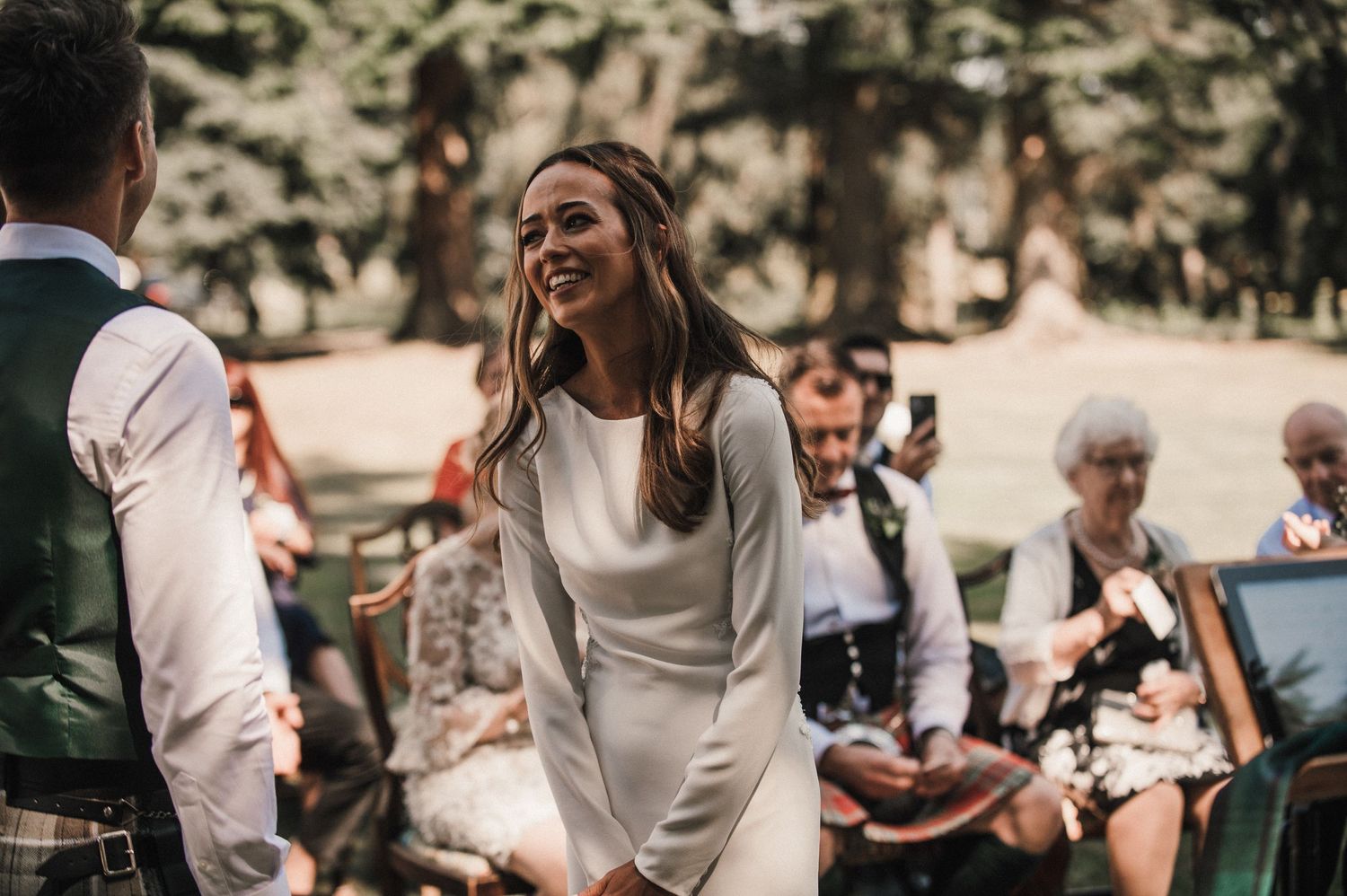A joyful moment captured during an outdoor wedding ceremony with guests watching in background.