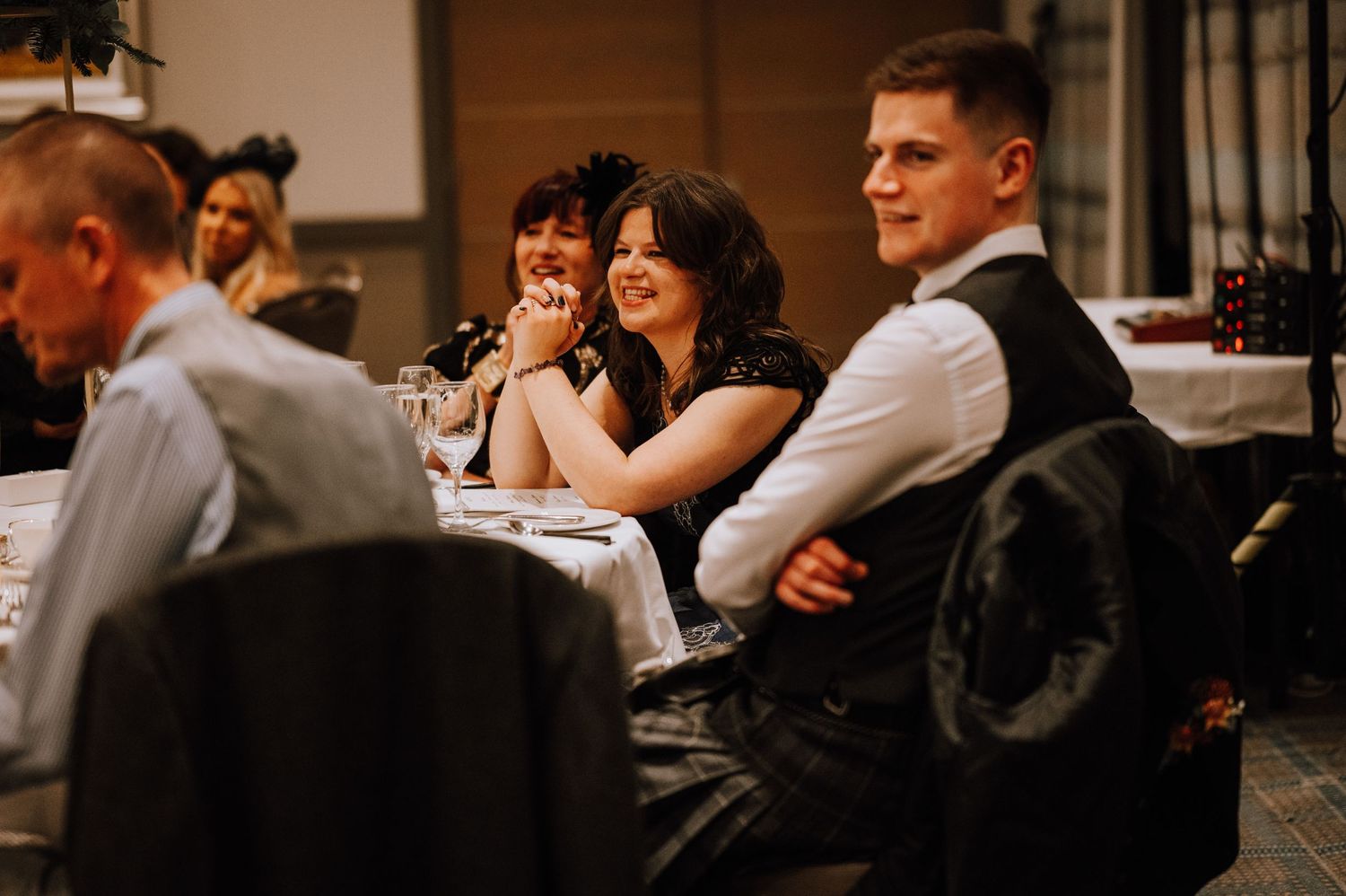 Wedding guests share laughs and conversations during an indoor reception dinner.