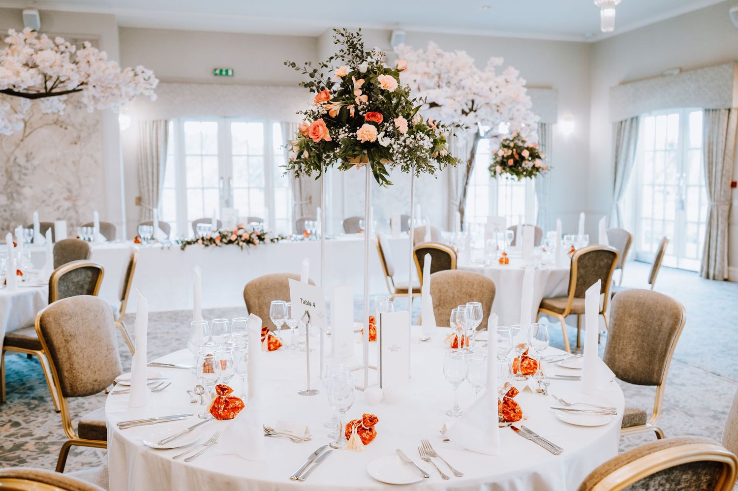 Luxurious wedding reception room with tall floral centerpieces and white table settings.
