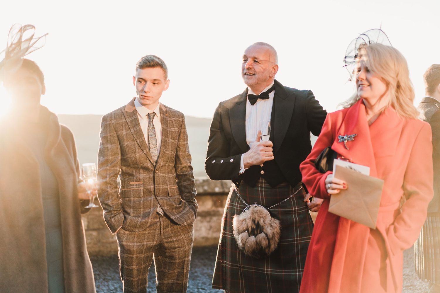 Wedding party in formal attire including traditional Scottish kilt poses at sunset.