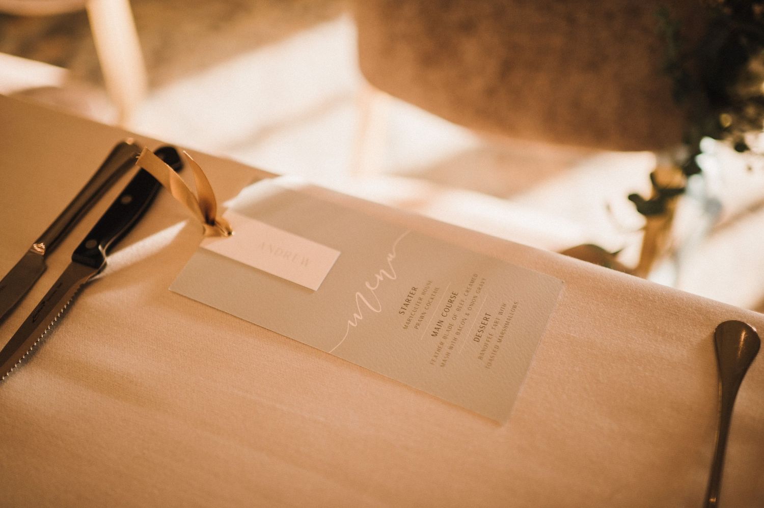 Minimalist wedding table setting with menu card and utensils in warm lighting.