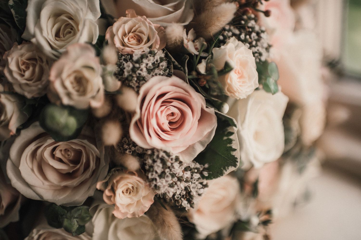 Detailed close-up of pale pink and cream roses with baby's breath in a wedding bouquet.