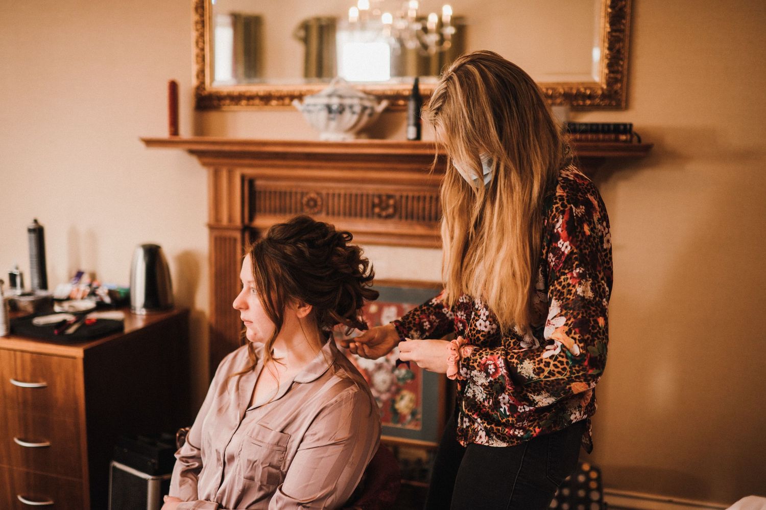 Stylist arranging client's hair in warm-toned room with ornate mirror.
